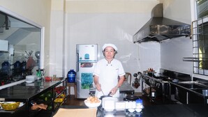 A chef in a kitchen with stainless steel appliances, a refrigerator, and a large window. - Than Thien Friendly Hotel (Hue)