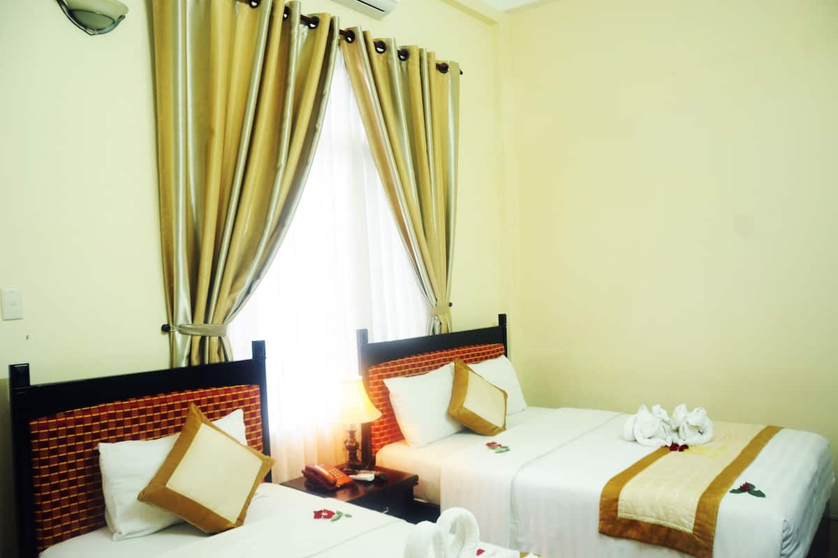 Habitación de hotel con dos camas, cabecera de ladrillo, ventana con cortinas y toallas sobre las camas.