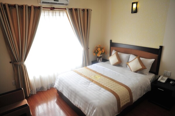 A hotel room with a large bed, a nightstand with a phone, and a window with curtains. - Than Thien Friendly Hotel (Hue)