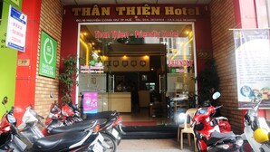 The exterior of Than Thien - Friendly Hotel with a red brick facade, a glass entrance, and several scooters parked in front. - Than Thien Friendly Hotel (Hue)