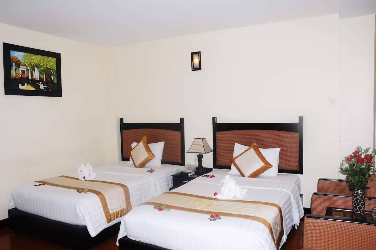 Una habitación de hotel con dos camas, una mesita de noche con lámpara, una pequeña mesa con un florero y un cuadro en la pared.