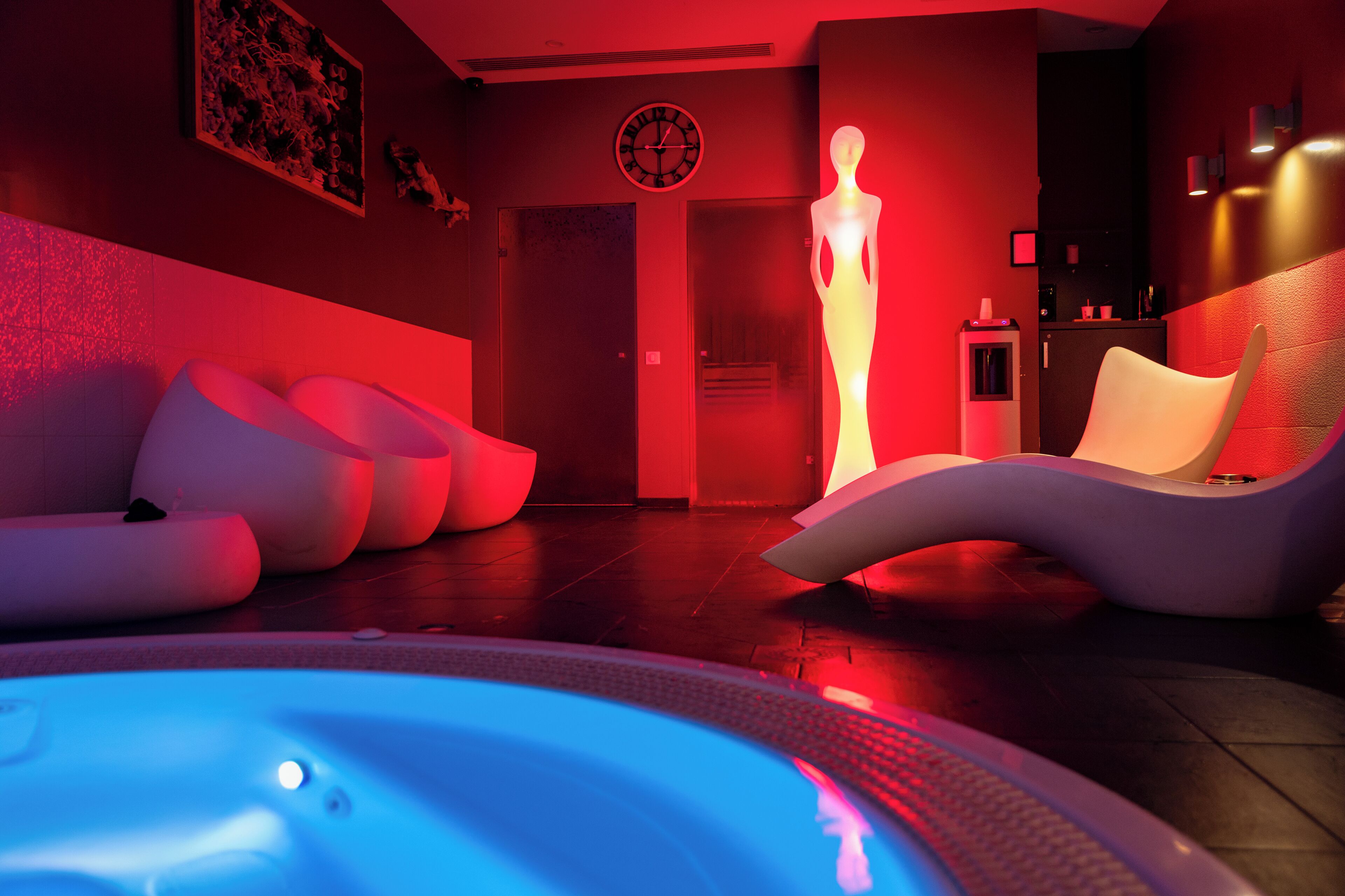 A modern spa area with a hot tub, white lounge chairs, and a wall-mounted clock.
