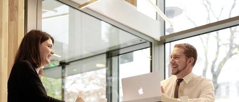 A modern office setting with a glass partition, wooden paneling, and a visible Apple laptop.
