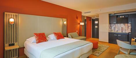 A hotel room with a large bed, a desk, and a kitchenette.