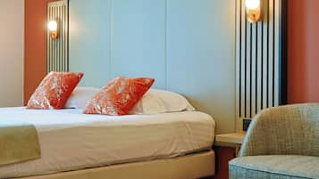 A hotel room with a bed, two pillows, a nightstand, and a chair.