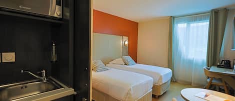 Une chambre d’hôtel avec deux lits, un bureau, une chaise, un lavabo et une fenêtre avec des rideaux.