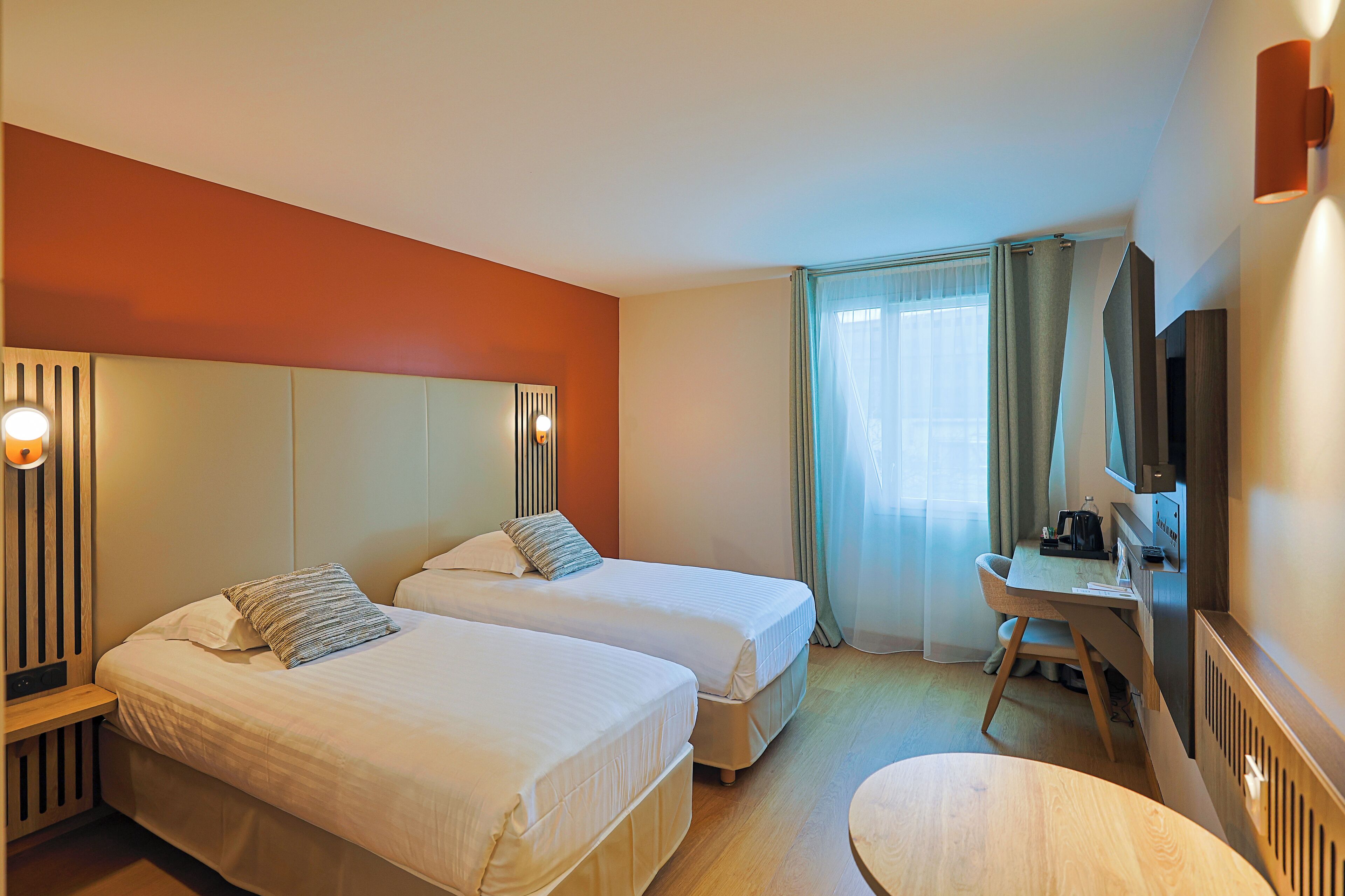Habitación de hotel con dos camas, un escritorio, una silla, un televisor y una ventana con cortinas.