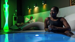 A person relaxing in a room with a massage chair and a pool area. - Seven Urban Suites Nantes Centre (Nantes)