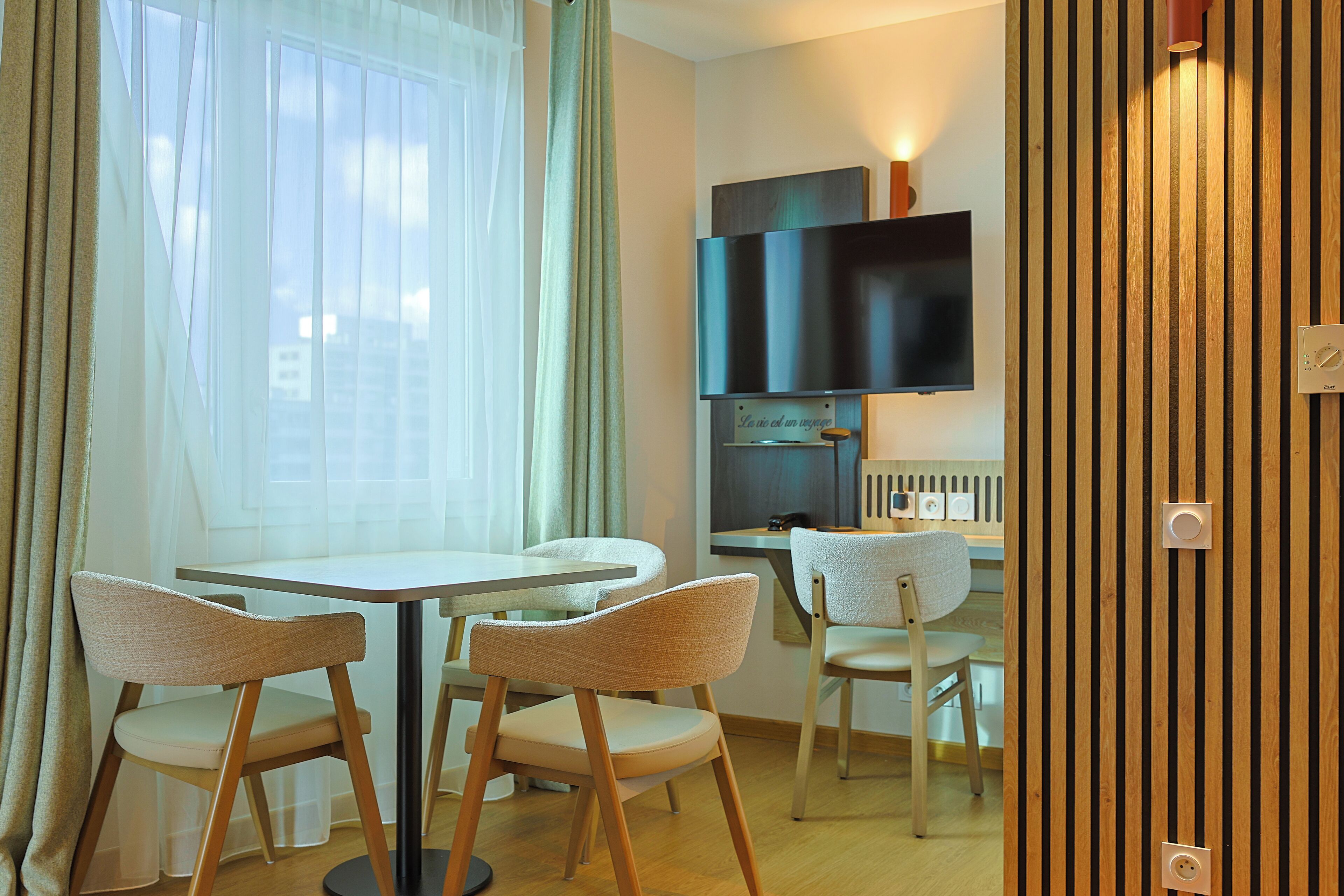 Un comedor con una mesa redonda y cuatro sillas, un televisor montado en la pared, y un panel de pared de madera.