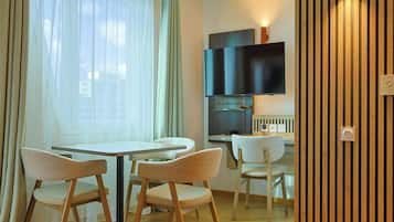 Un comedor con una mesa redonda y cuatro sillas, un televisor montado en la pared, y un panel de pared de madera.