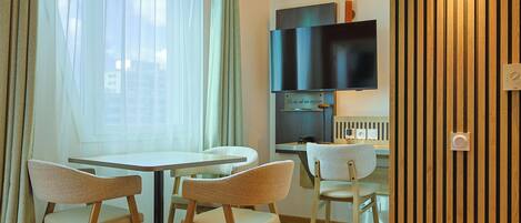 Un coin repas avec une table ronde et quatre chaises, un téléviseur fixé au mur et un mur recouvert de panneaux en bois.