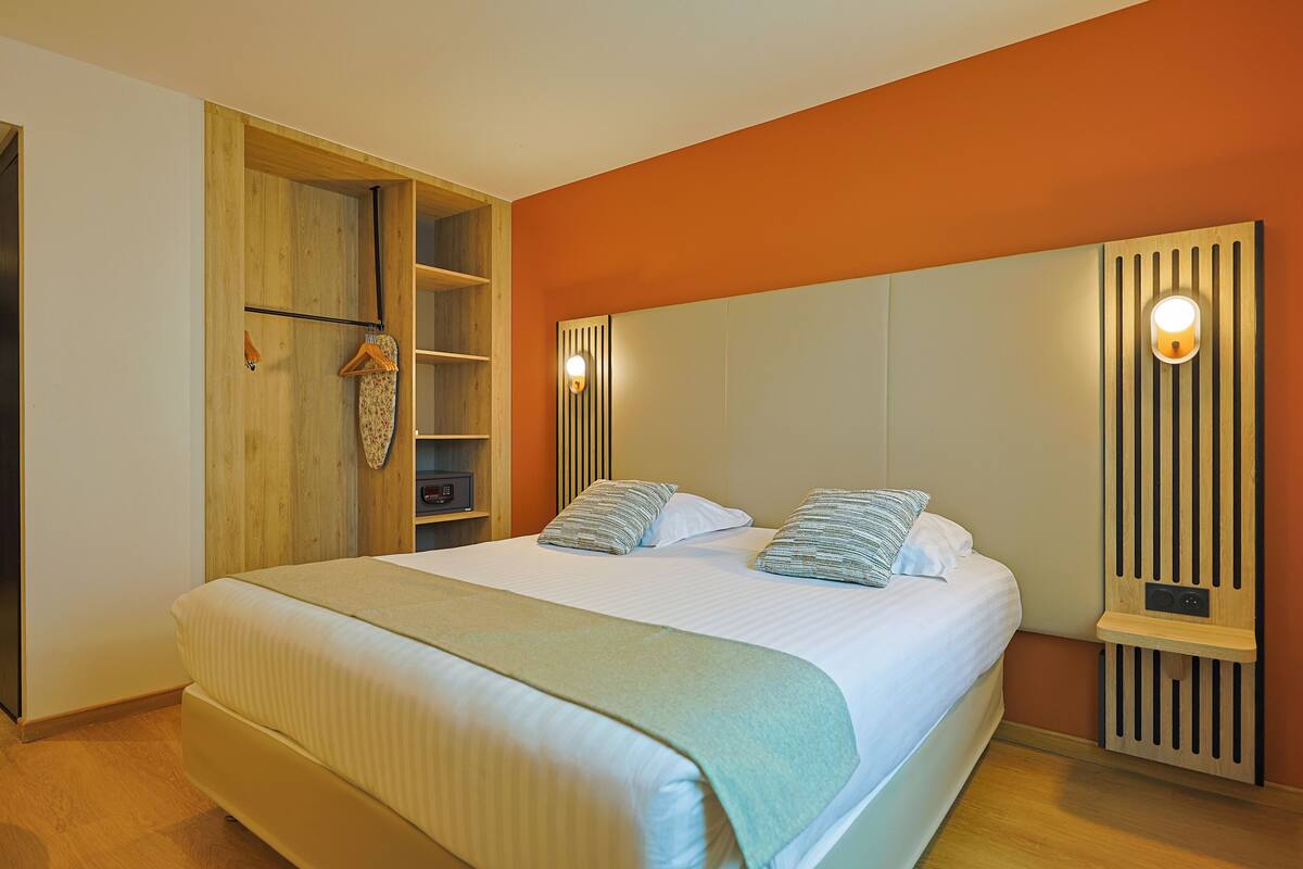 Een slaapkamer met een bed, een houten garderobe, een plankunit en een wandlamp.