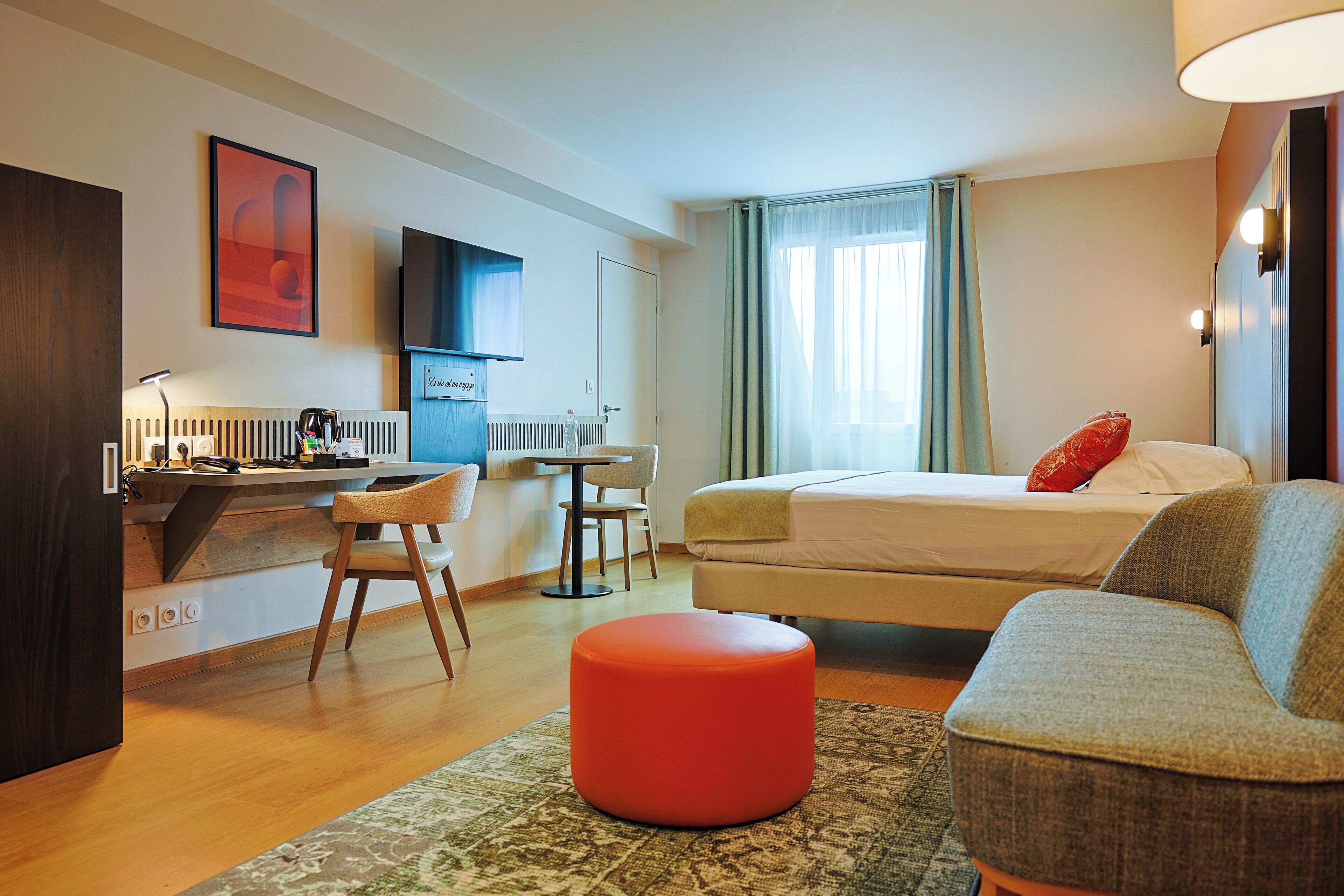 Una habitación de hotel con una cama, un escritorio con una silla, un televisor y una ventana con cortinas.