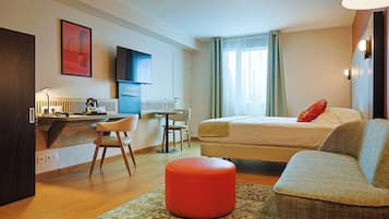 Una habitación de hotel con una cama, un escritorio con una silla, un televisor y una ventana con cortinas.