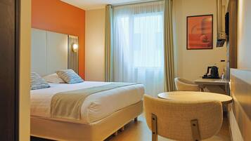 A hotel room with a bed, a desk, a chair, and a window with curtains.