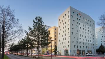 Un hôtel moderne à plusieurs étages, avec une enseigne bien visible indiquant « seven urban », et une vue dégagée sur la rue au premier plan.