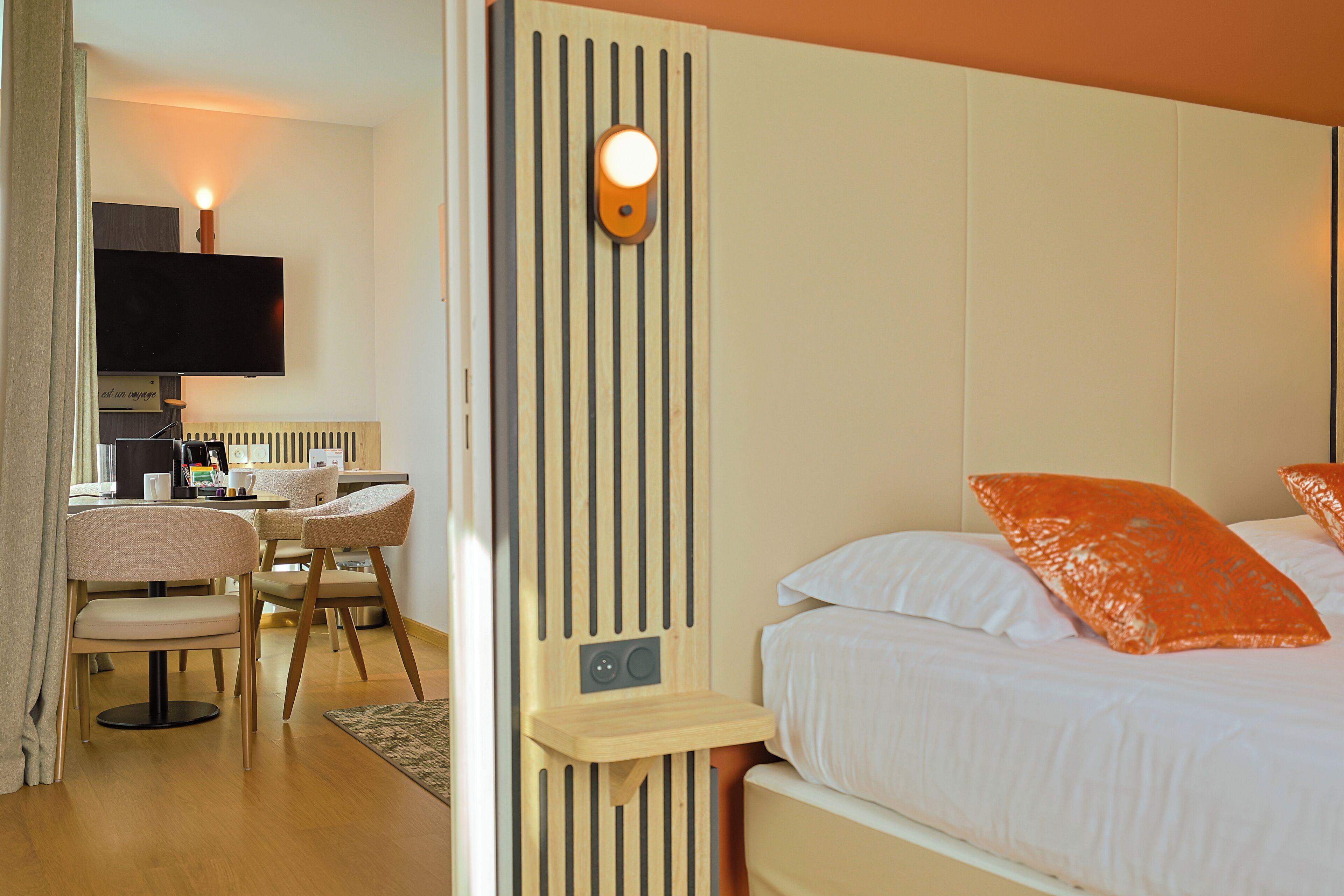 Habitación de hotel con una cama, un escritorio con silla, un televisor y una lámpara fijada a la pared.