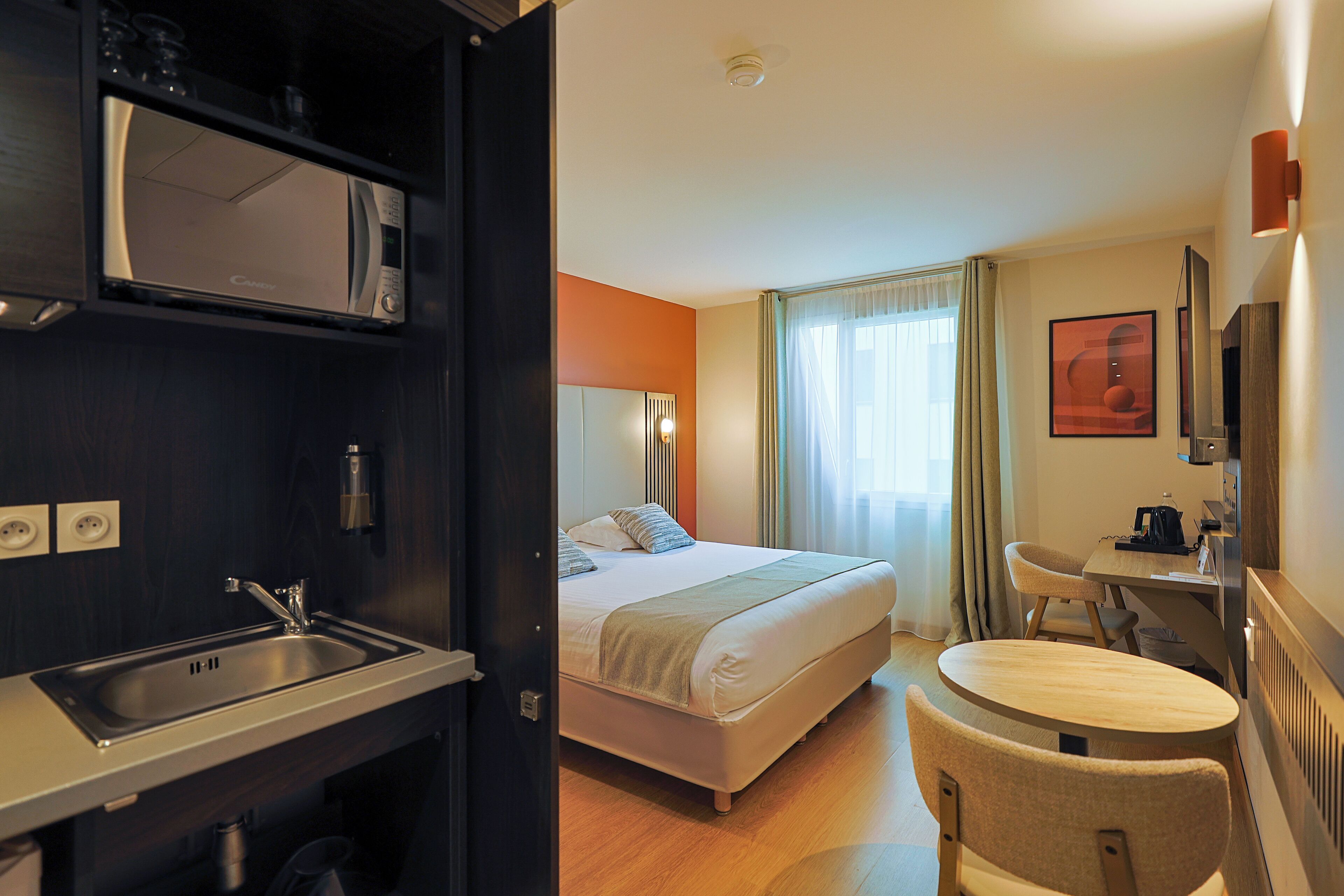 A hotel room with a bed, a desk, a chair, a sink, and a microwave.