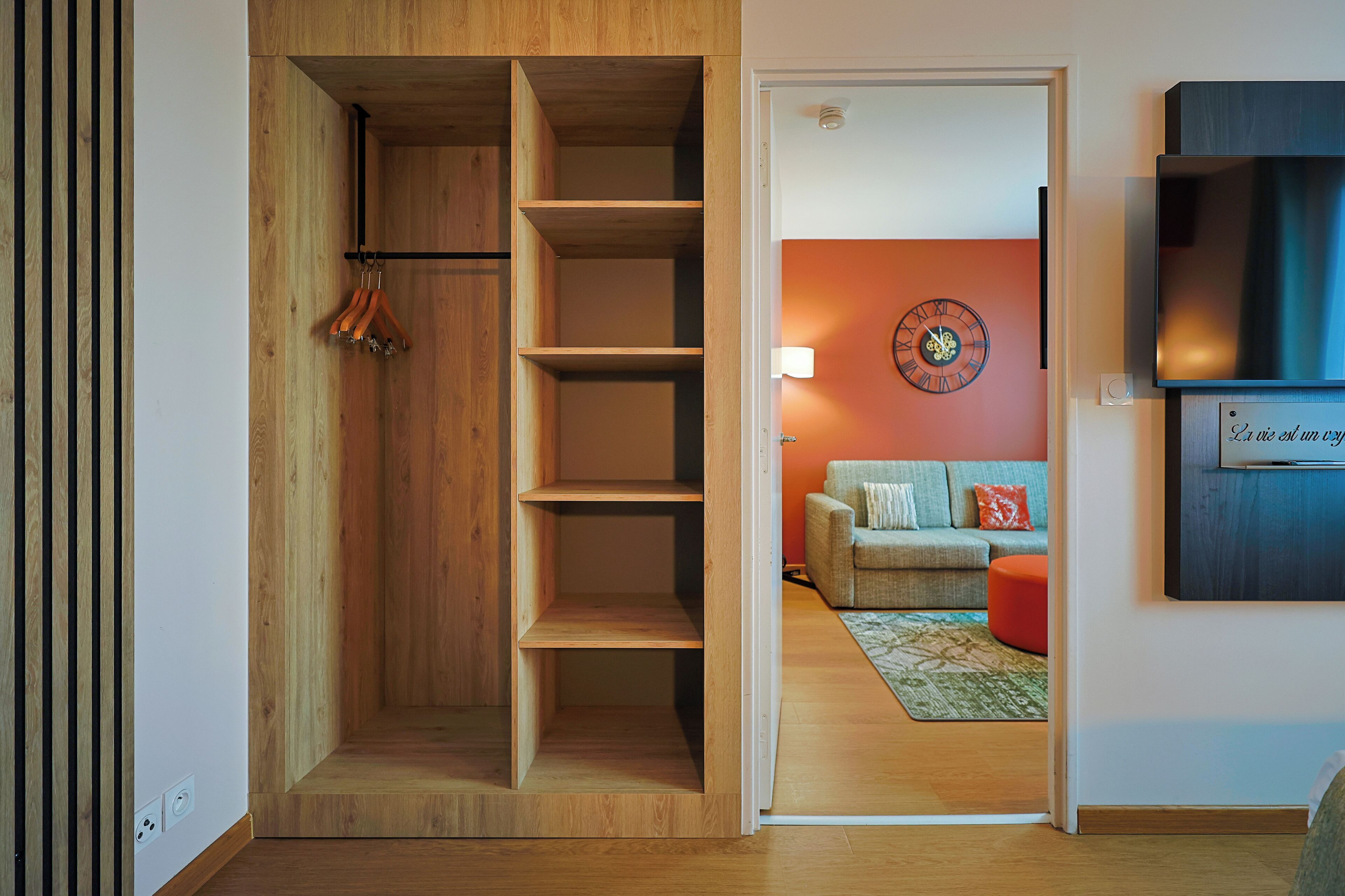 Un intérieur moderne avec une étagère en bois, un ensemble de canapés et un téléviseur fixé au mur.