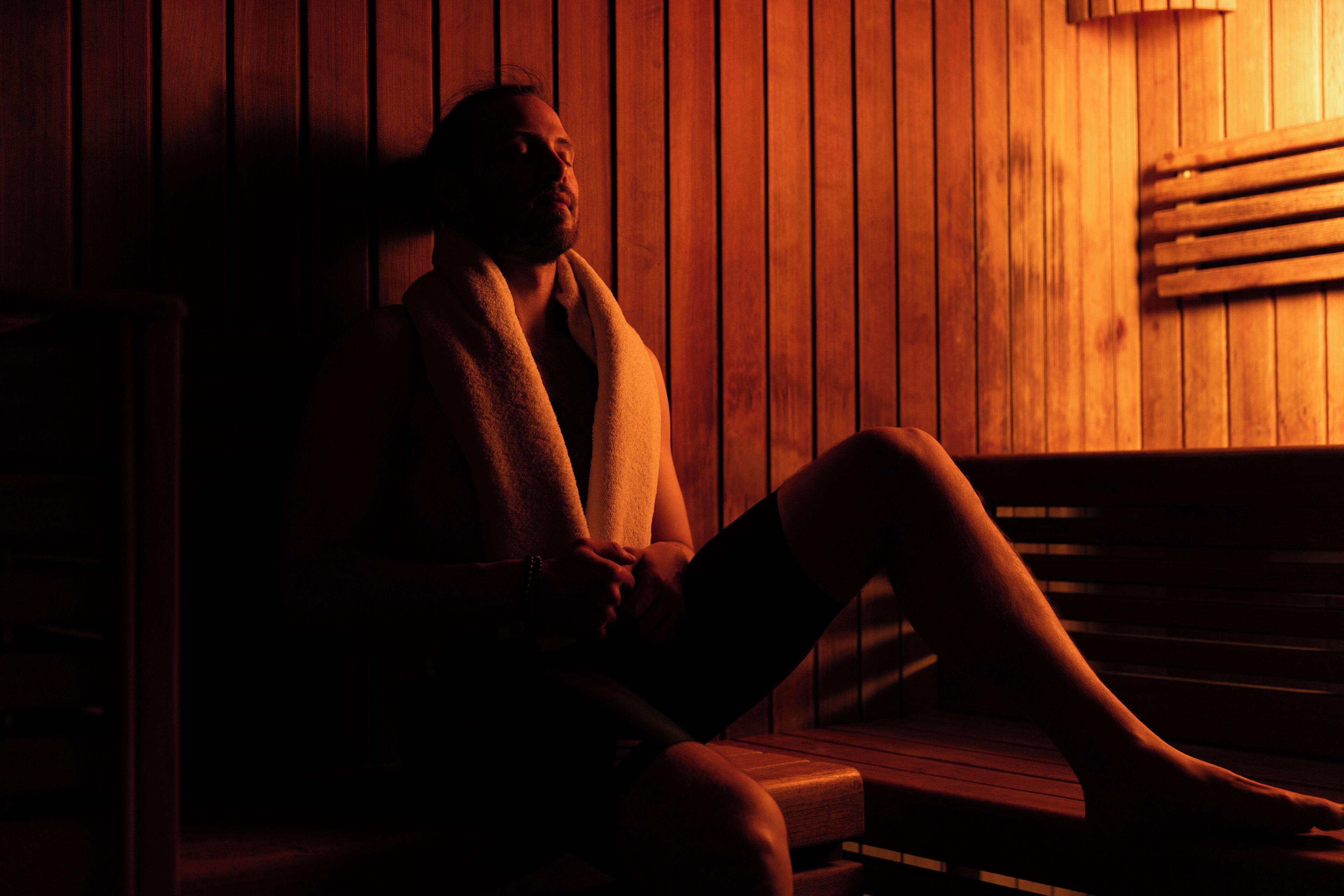 A person sitting in a wooden sauna with a bench and a slatted wall.