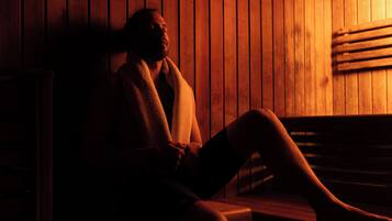 A person sitting in a wooden sauna with a bench and a slatted wall.