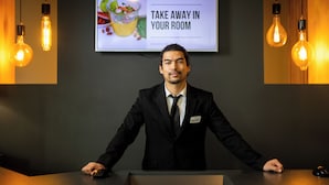 A man in a suit standing behind a podium with a screen above displaying a message. - Seven Urban Suites Nantes Centre (Nantes)