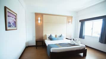 Habitación de hotel con cama, mesita de noche, lámpara de pared, ventana con cortinas y un cuadro en la pared.