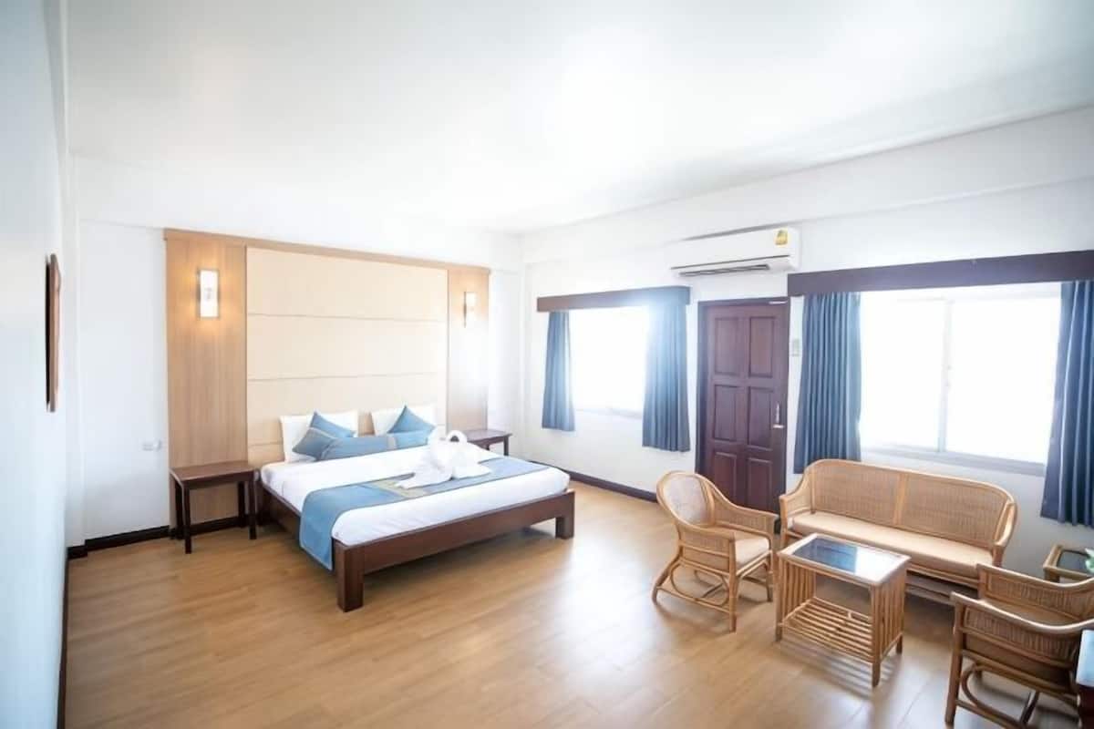 A hotel room with a bed, a sofa, a chair, a small table, and a window with curtains.