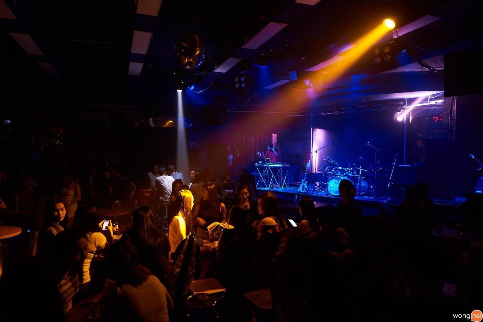 A crowded indoor venue with a stage and musical equipment, suggesting a live music event.