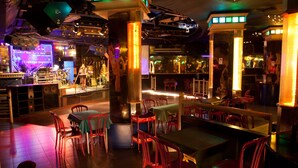 Een restaurant met rode stoelen, tafels en een podium met muziekinstrumenten.
