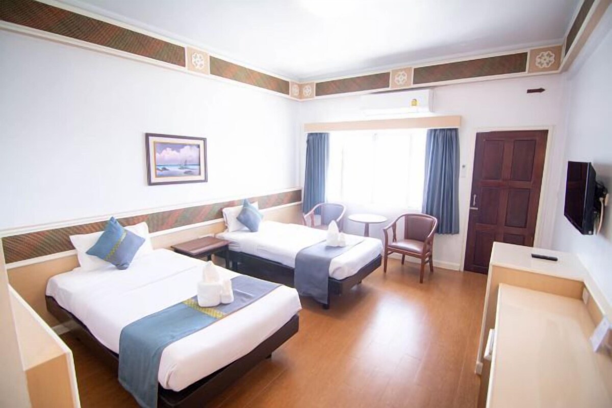 A hotel room with two beds, a desk, a chair, a TV, and a window with curtains.