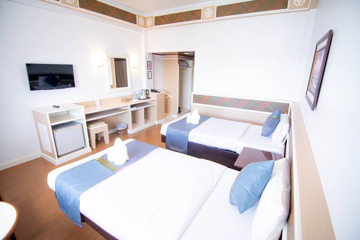 A hotel room with two beds, a TV, a desk, and a small kitchenette.