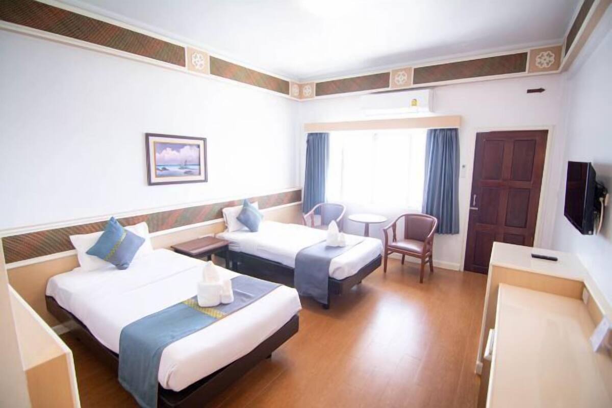 A hotel room with two beds, a desk, a chair, a TV, and a window with curtains.