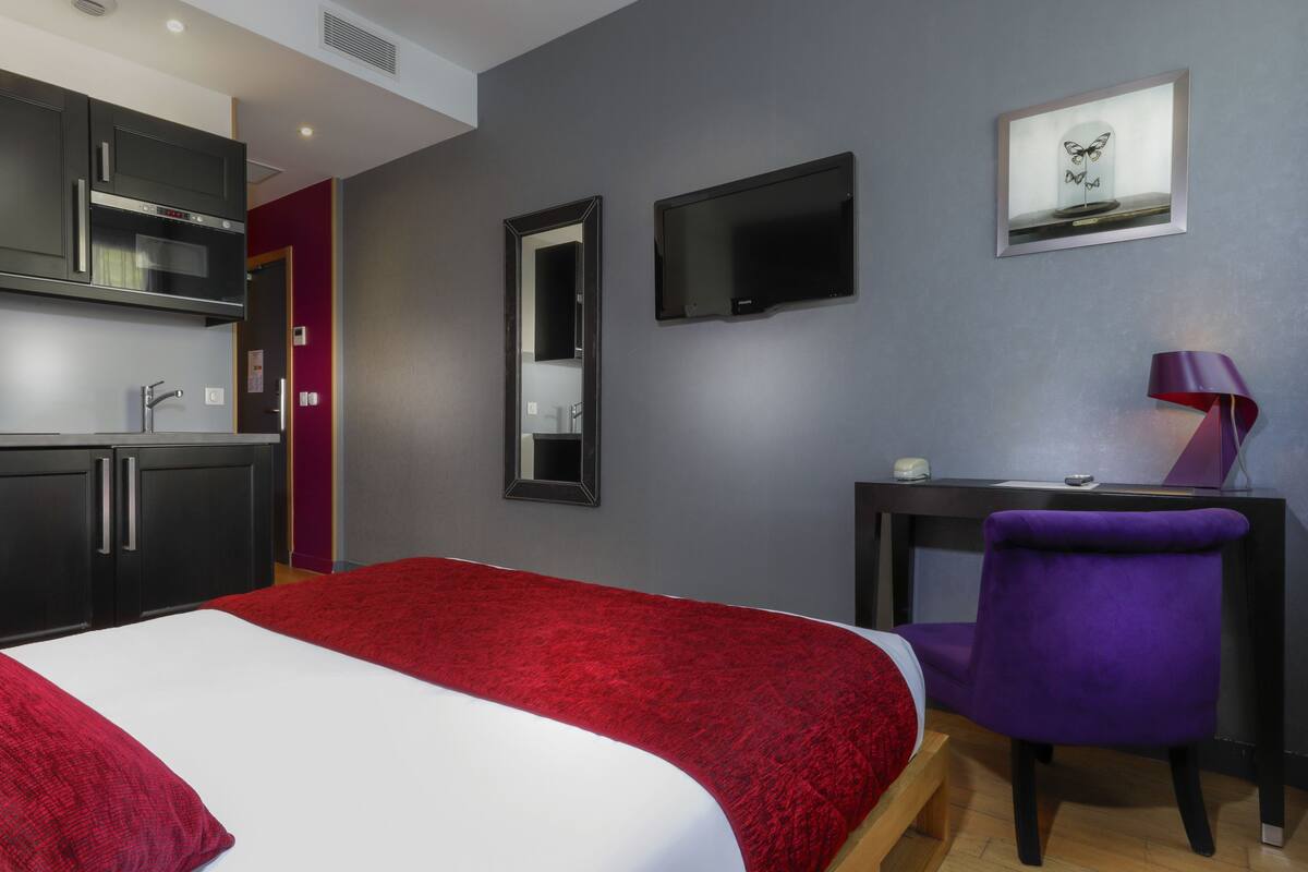 A hotel room with a bed, a desk, a chair, a TV, and a mirror.