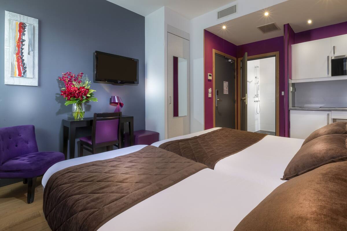 A hotel room with a bed, a desk, a chair, a TV, and a shower area.