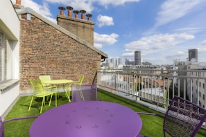 A rooftop terrace with a brick wall, a round table, and chairs, overlooking a cityscape. - Hotel Ambre (Paris)