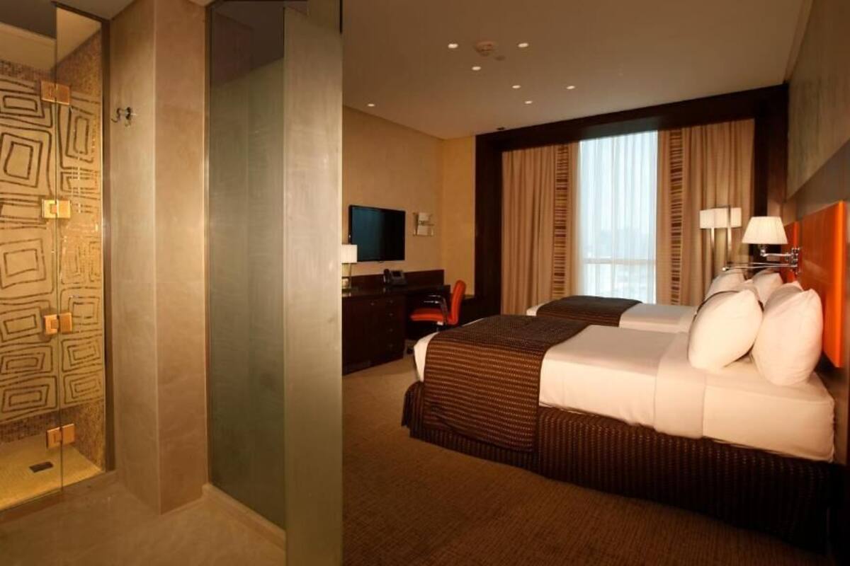 A hotel room with a shower, a bed with pillows, a TV, and a desk with a chair.