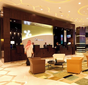 A hotel reception area with a modern design, including a reception desk, seating area, and a television screen.