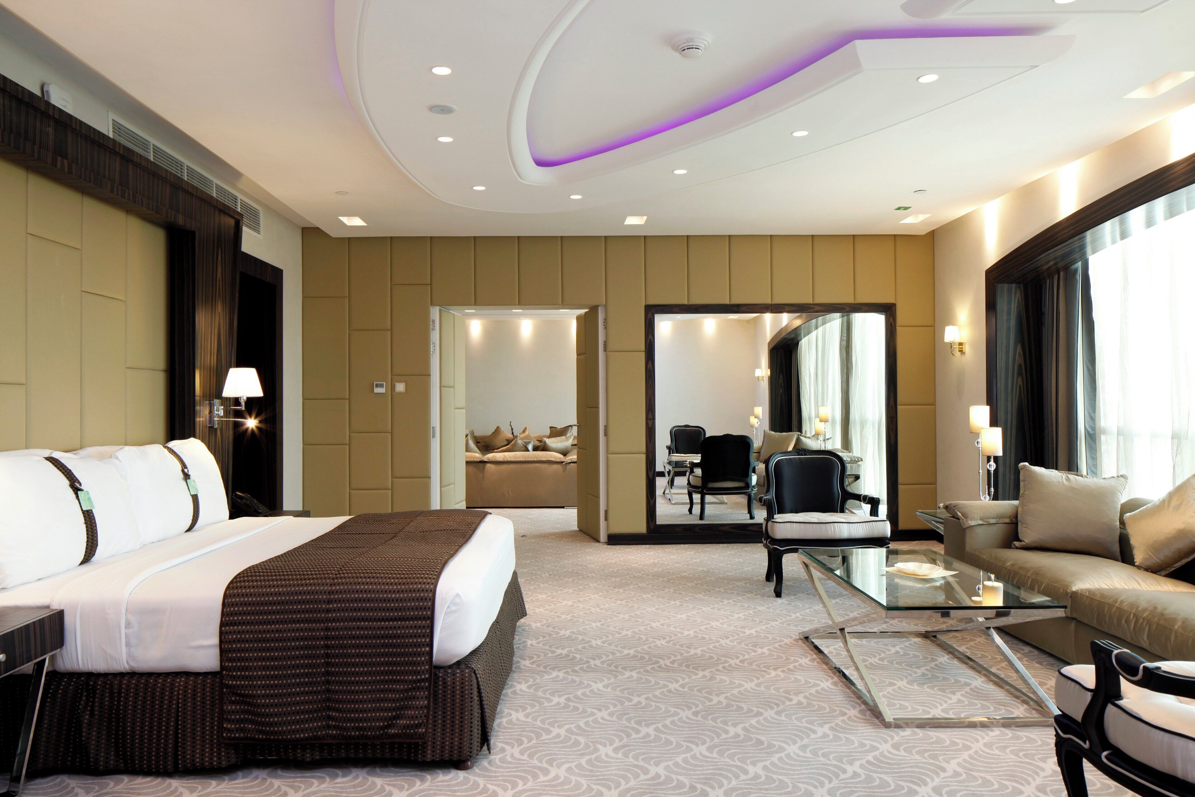 A hotel room with a large bed, a sofa, a coffee table, and a seating area with chairs.