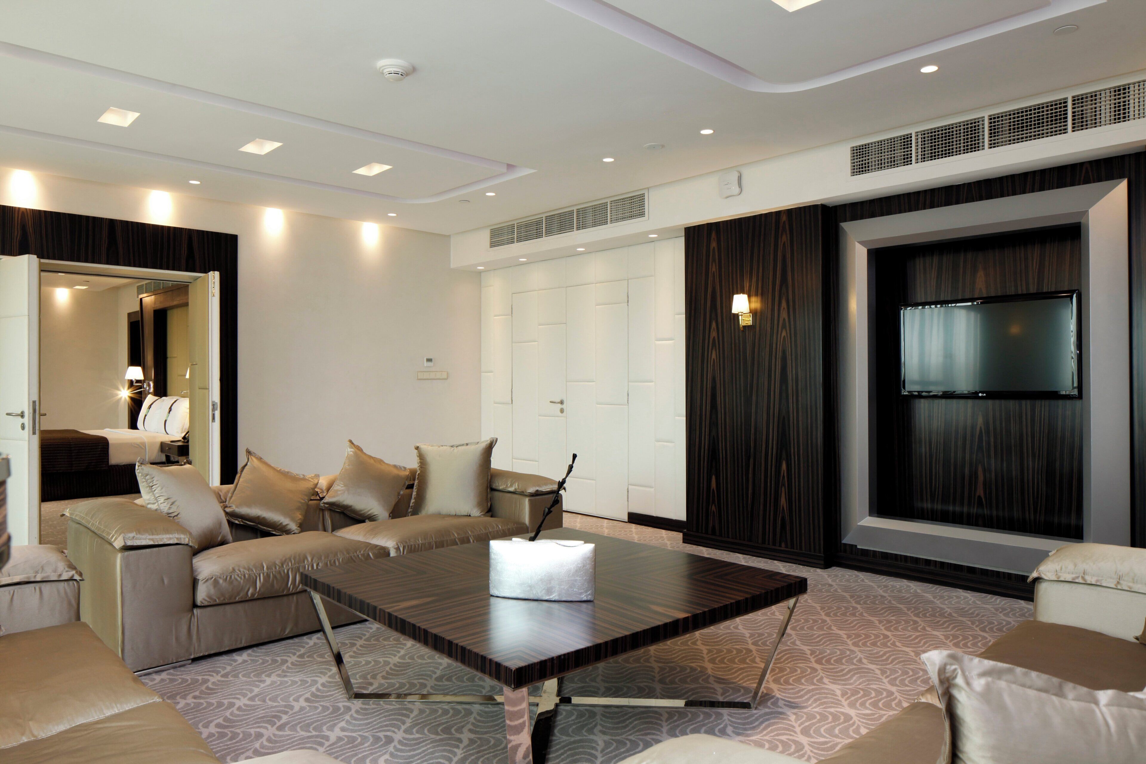 Habitación de hotel moderna con un televisor de pantalla plana grande, un conjunto de sofás, una mesa de comedor y una alfombra estampada.