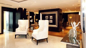 A spacious lobby with two white armchairs, a polished marble floor, and a decorative shell on a glass table.
