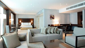 A modern hotel room with a large bed, a sofa, a desk, and a chair. There are two lamps on the desk and a painting on the wall.