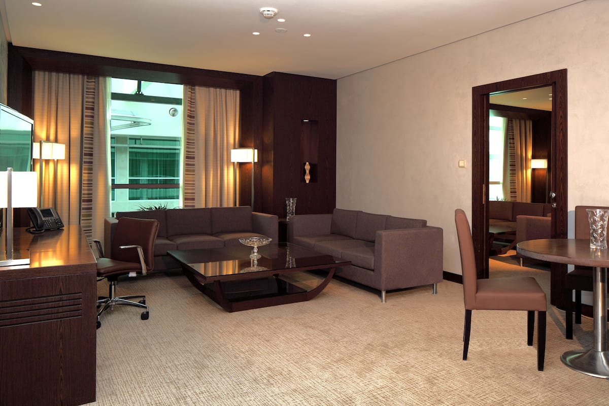 A hotel room with a sofa, a coffee table, a desk with a phone, a chair, and a dining table with chairs.