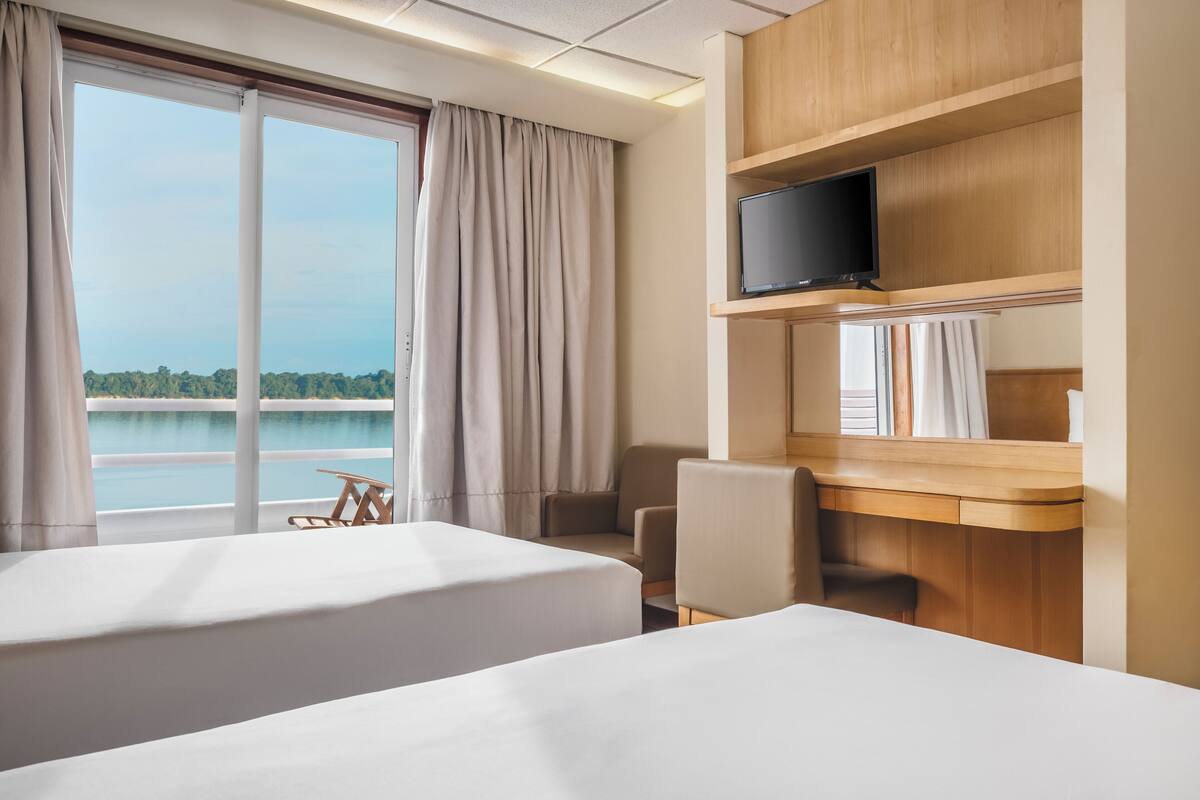 Habitación de hotel con dos camas, un escritorio, una silla, un televisor y vistas a un lago.