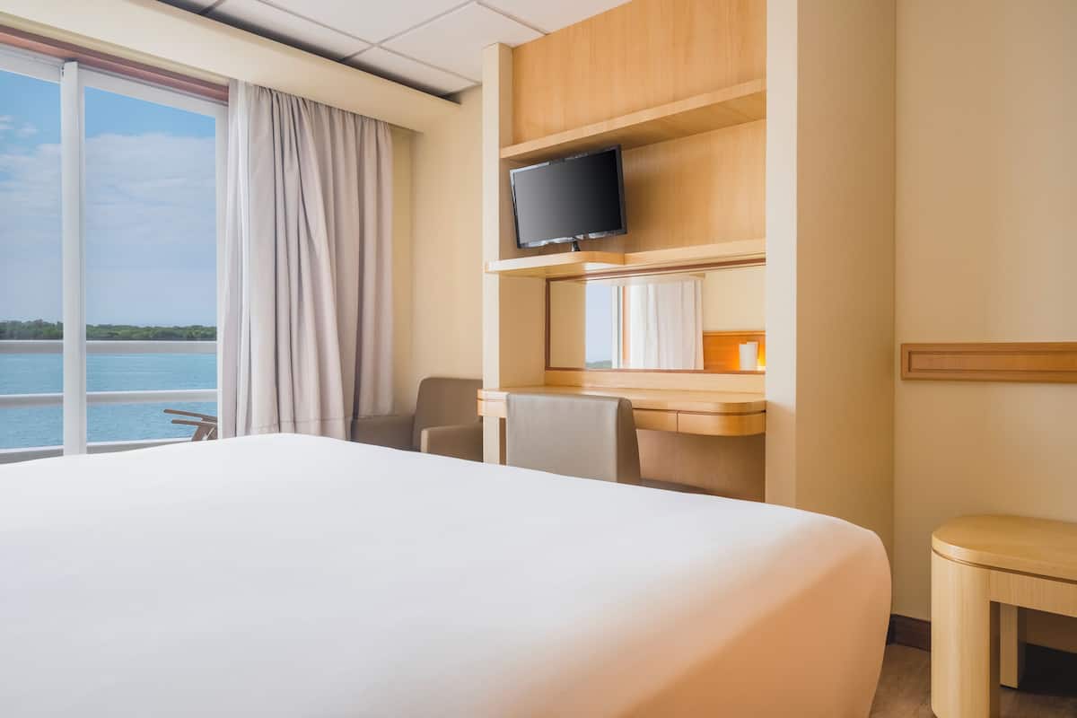 Habitación de hotel con una cama grande, un escritorio, un televisor de pantalla plana, una silla y vista al mar.