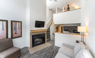 Una sala de estar moderna con chimenea, un sofá, un televisor montado en la pared y una escalera que conduce a un nivel superior.