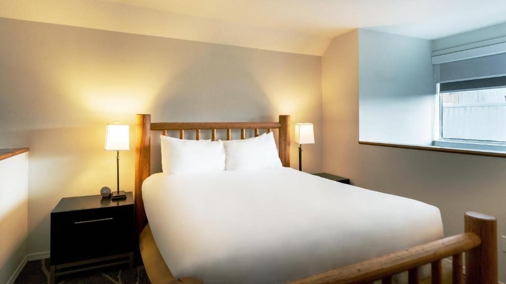 Ein Hotelzimmer mit einem Bett, Nachttischlampen, einem Nachttisch und einem Fenster.