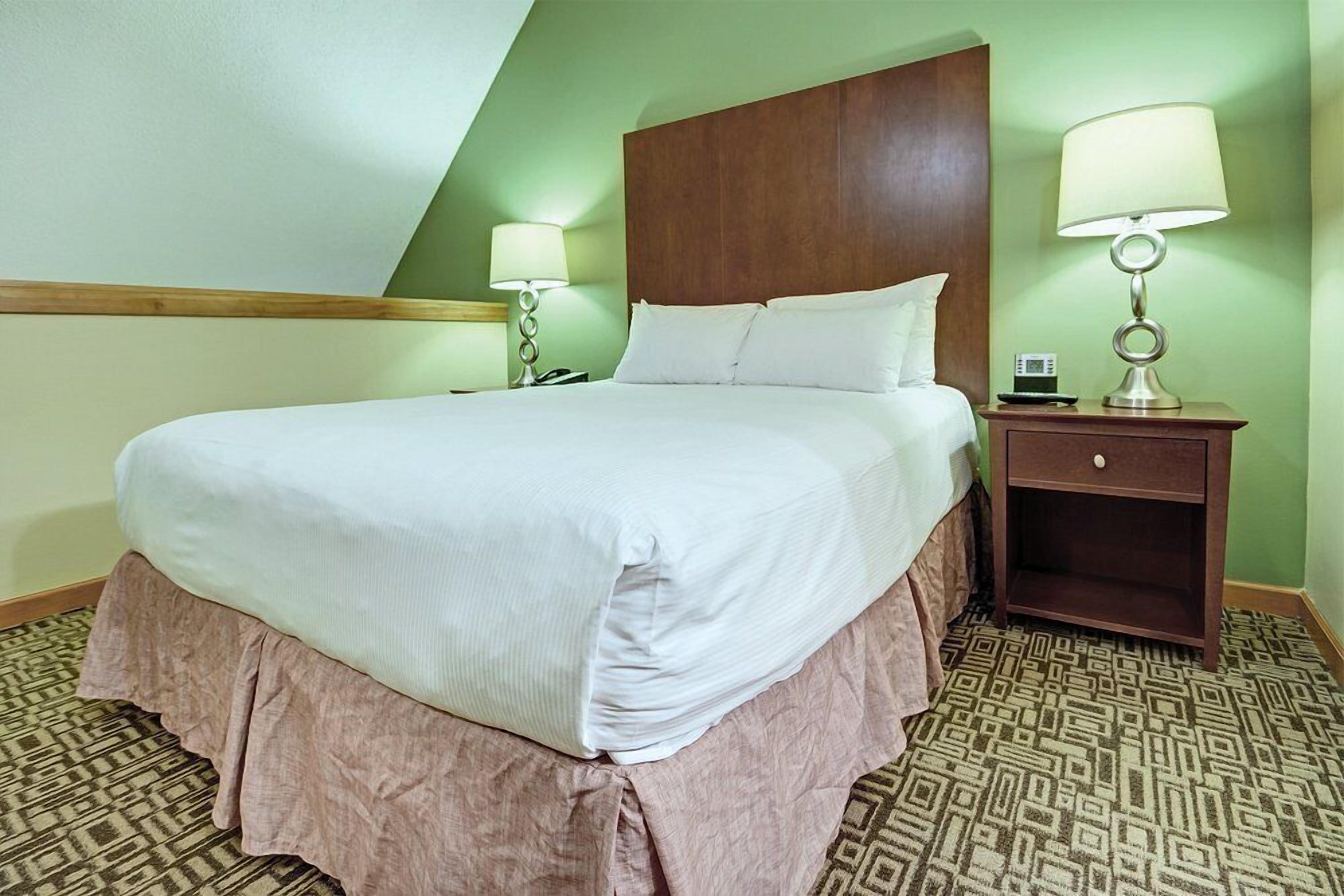 A hotel room with a large bed, two bedside tables, a wooden headboard, and patterned carpet.