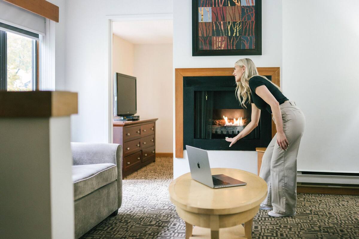 Una sala de estar con chimenea, un sofá, un televisor y una laptop sobre una mesita.