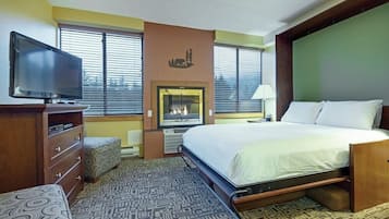 Una habitación de hotel con cama, televisión, chimenea y ventana con persianas.